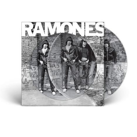 "RAMONES" in großen weißen Buchstaben oben. Vier Personen in Lederjacken vor einer Ziegelmauer mit Graffiti.