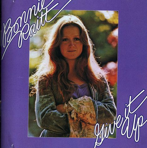 „Bonnie Raitt“ und „Give it Up“ in geschwungener Schrift auf violettem Hintergrund. Eine Frau in der Mitte, lächelt.