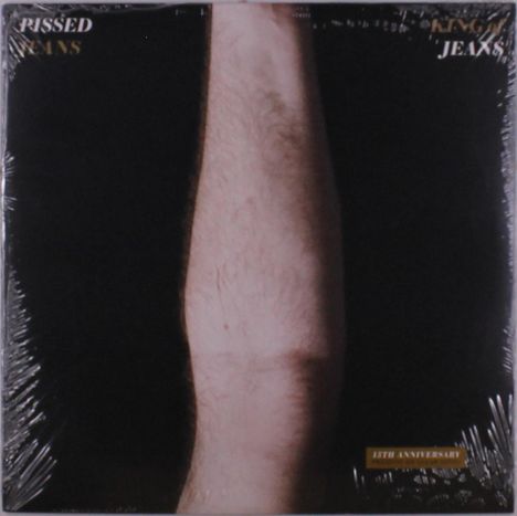 "PISSED JEANS" und "KING OF JEANS" in weißem Text, darunter ein Arm auf schwarzem Hintergrund, 13th Anniversary Edition.