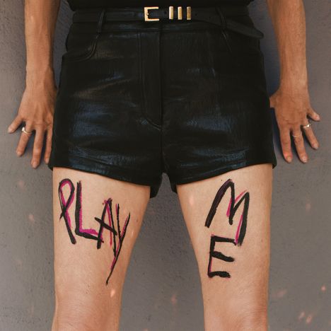 "PLAY ME" steht auf den Schenkeln einer Person in schwarzen Ledershorts geschrieben.