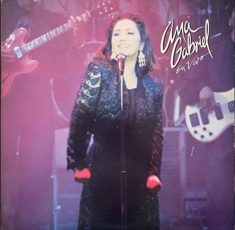 Der Text lautet "Ana Gabriel En Vivo". Eine Sängerin auf der Bühne mit Mikrofon, sie trägt ein schwarzes Outfit; Musiker im Hintergrund.