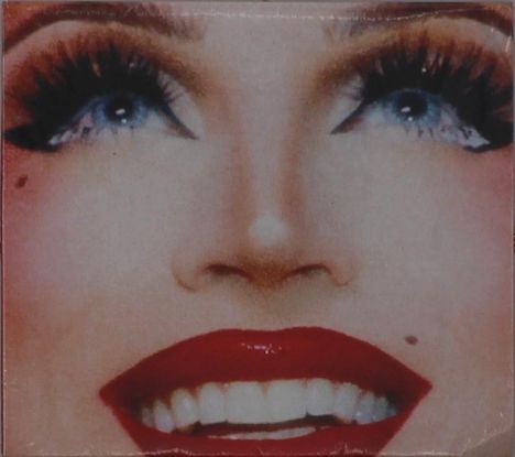 Eine Nahaufnahme eines Gesichts mit roten Lippen, blauen Augen und stark geschminkten Wimpern, mit Schönheitsfleck.