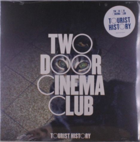 Text: "TWO DOOR CINEMA CLUB", "TOURIST HISTORY". Schwarzer Hintergrund, Katze im Bild, geometrisches Fliesenmuster.