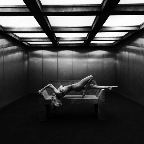 Kein Text vorhanden. Ein Raum mit heller Decke, eine Person liegt auf einem Tisch in einer kunstvollen, verdrehten Pose.
