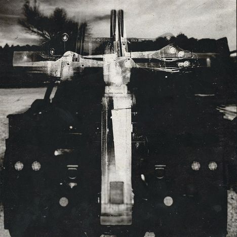 Doppelt belichtete Schwarz-Weiß-Ansicht einer mechanischen Struktur, die einem Kreuz ähnelt, vor unscharfem Hintergrund.