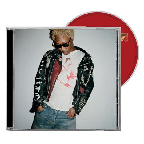 Ein Mann mit blonden Haaren trägt eine Nietenlederjacke, Sonnenbrille, weißes Shirt mit rotem Print und Jeans.