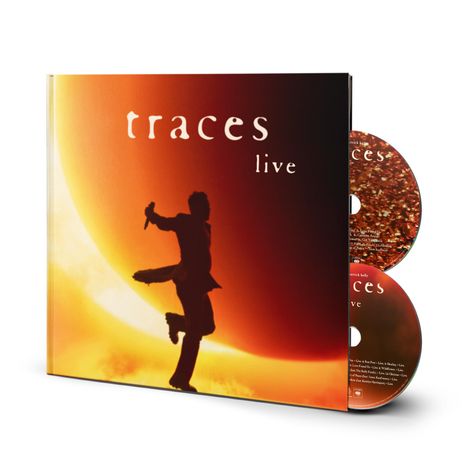 Der Text "traces live" steht im Vordergrund. Eine Silhouette einer Person mit Mikrofon springt vor einem leuchtend orangen Hintergrund.