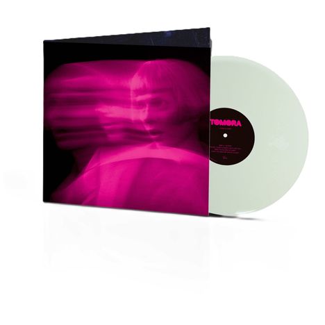 Text "TOMORA" auf einer Plattenhülle. Darauf ein verwischtes, pinkes Bild eines Gesichts. Weiße Vinyl-Schallplatte.