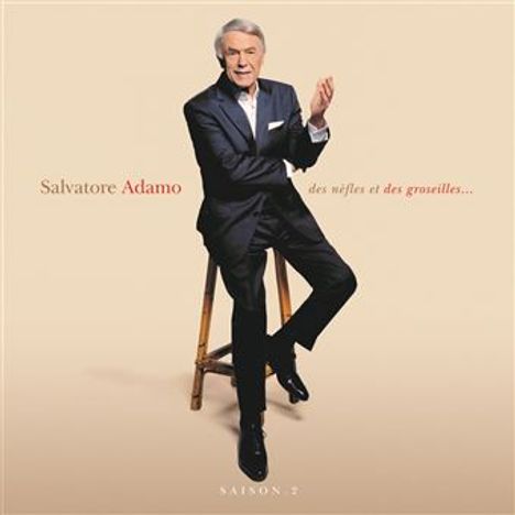 "Salvatore Adamo, des nèfles et des groseilles... Saison 2." Ein Mann in Anzug sitzt auf einem Hocker vor hellem Hintergrund.