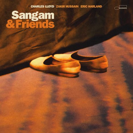 Oben stehen die Namen Charles Lloyd, Zakir Hussain, Eric Harland. Darunter „Sangam & Friends“. Im Vordergrund liegen Schuhe.