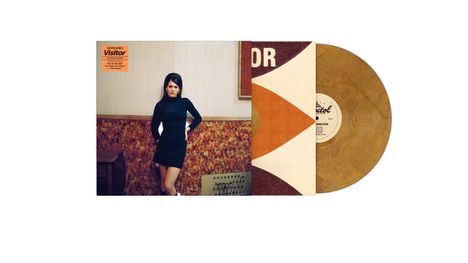 Text: „Sienna Spiro, Visitor.“ Eine Frau in einem schwarzen Kleid steht vor einer gemusterten Wand. Daneben eine goldene Vinyl.