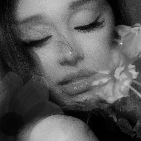 Eine Frau mit geschlossenen Augen in Nahaufnahme, umgeben von Blumen in Schwarzweiß.