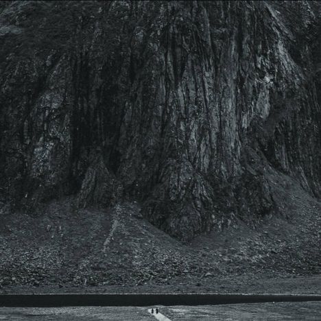 Eine vertikale Linie aus Schrauben auf hellem Untergrund, unten ein schwarzes Rechteck.