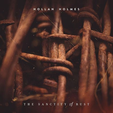 Text: "HOLLAN HOLMES", "THE SANCTITY of RUST". Nahaufnahme von rostigen, ineinander verwobenen Metallstücken.