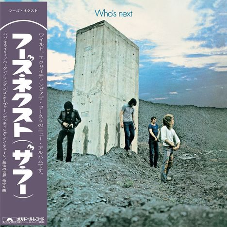 Text oben: "Who's next". Vier Männer stehen vor einem großen Betonblock in einer kargen Landschaft unter bewölktem Himmel.