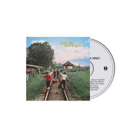 "ARE WE GONNA SING?" in gelber Schrift auf einem Albumcover. Drei Personen gehen Hand in Hand auf Bahngleisen.