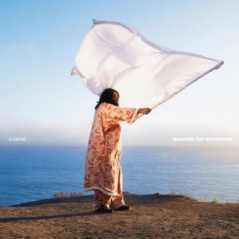 Text: "ELMIENE" und "sounds for someone". Person in buntem Gewand hält ein großes Tuch am Meer.