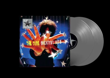 "The Cure Greatest Hits" steht in gelber und weißer Schrift. Eine Hand streckt sich dem Betrachter entgegen, umgeben von Sternen.
