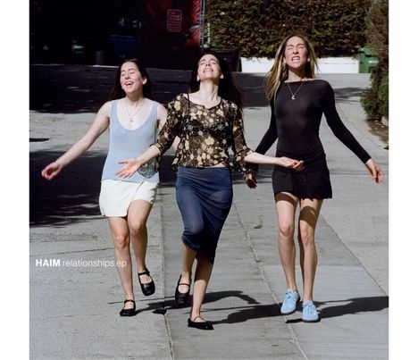 Drei Frauen gehen fröhlich eine Straße hinunter. Links steht "HAIM relationships ep". Alle wirken ausgelassen.