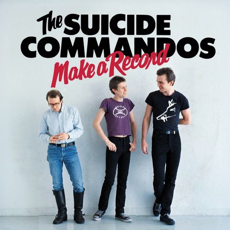 Text: "The Suicide Commandos Make a Record." Drei Männer stehen lächelnd nebeneinander an einer weißen Wand.