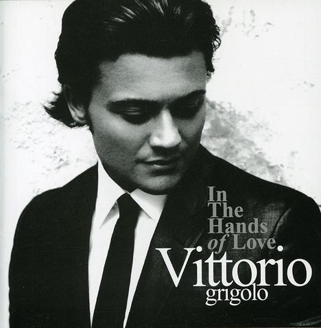 Text: "In The Hands of Love. Vittorio grigolo". Ein Mann in Anzug und Krawatte schaut nach unten, monochromes Porträt.