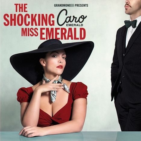 "The Shocking Miss Emerald", "Caro Emerald", stilvolle Frau in rotem Kleid und schwarzem Hut, neben Mann im Anzug.