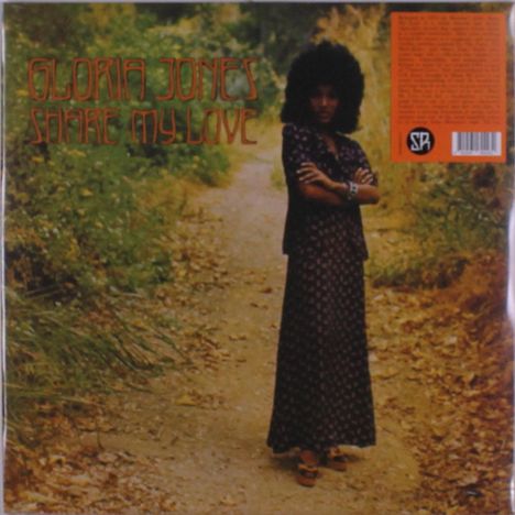 "Gloria Jones Share My Love." Eine Frau steht mit verschränkten Armen auf einem Pfad, umgeben von viel Laub.