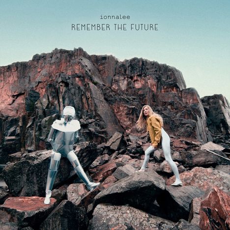 Text: "ionnalee REMEMBER THE FUTURE". Zwei Personen, eine in silbernem Anzug, eine in gelbem Oberteil, auf Felsen.