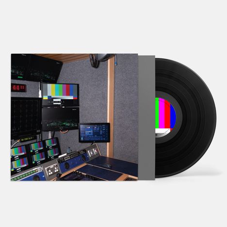 Monitore mit Testbildern und Kontrollbildschirme in einem Tonstudio. Eine schwarze Schallplatte ist teilweise sichtbar.