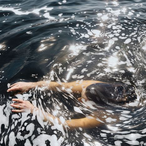 Eine Person schwimmt im Wasser, umgeben von Schaum und Sonnenlicht, das sich auf der Wasseroberfläche spiegelt.