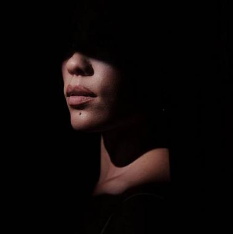 Der untere Teil eines Gesichts im Schatten, mit betonten Lippen und einem markanten Muttermal.