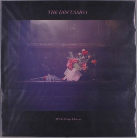 Die Schriftzüge „THE DISCUSSION“ und „All The Pretty Flowers“. Ein Blumenstrauß steht in einer Vase auf einer dunklen Oberfläche.