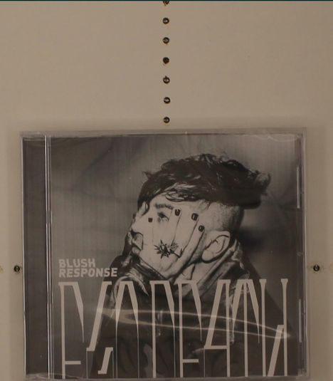 Text: "Blush Response". Schwarz-weißes CD-Cover mit einer Person, die das Gesicht mit einer Hand bedeckt.