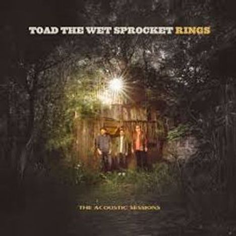 „TOAD THE WET SPROCKET RINGS“ und „THE ACOUSTIC SESSIONS“. Drei Personen stehen vor einer beleuchteten Hütte im Wald.