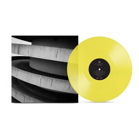 Schwarze Scheibe mit Text, gelbe Schallplatte. Graues Betongebäude mit Rundungen auf dem Cover.