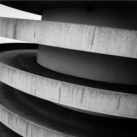Spiralrampe aus Beton mit grober Textur, die sich um eine zentrale Säule windet, schwarz-weiß fotografiert.
