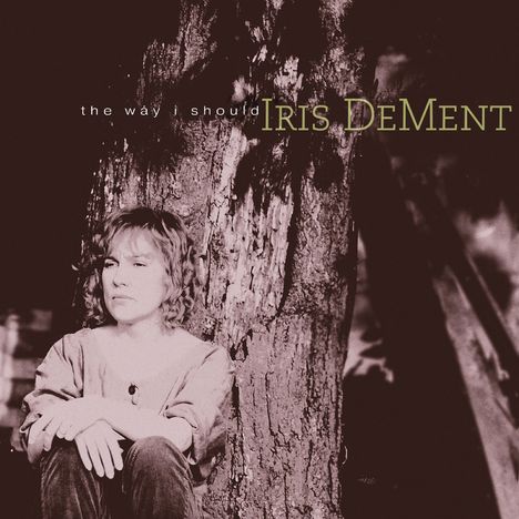 Text: "the way i should" und "IRIS DeMENT". Eine Person sitzt nachdenklich an einen Baum gelehnt. Monochromes Bild.