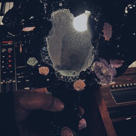 Ein Handspiegel mit blumigem Muster, gehalten vor einem Tascam-Gerät mit verschiedenen Knöpfen und Lichtern.