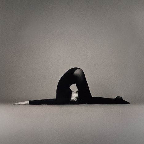Ein Mensch in schwarzer Kleidung macht eine Yoga-Pose auf grauem Hintergrund. Der Rücken ist stark gebogen.