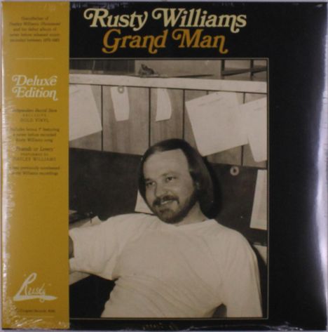 "Rusty Williams Grand Man", "Deluxe Edition". Sepia-Foto eines Mannes mit Hemd, umgeben von aufgehängten Papieren in Holzzaun.