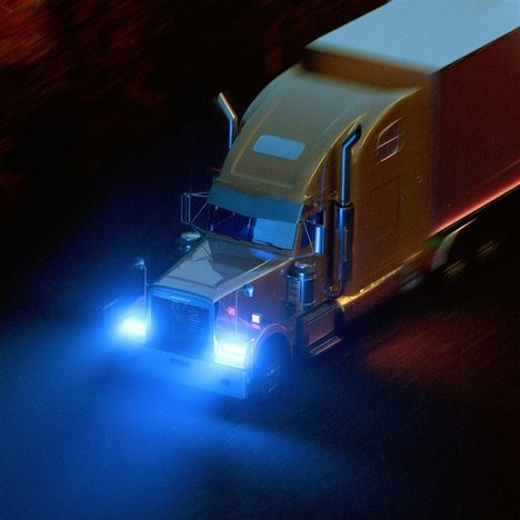 Ich sehe keinen Text. Ein Lastwagen mit leuchtenden blauen Scheinwerfern fährt nachts.