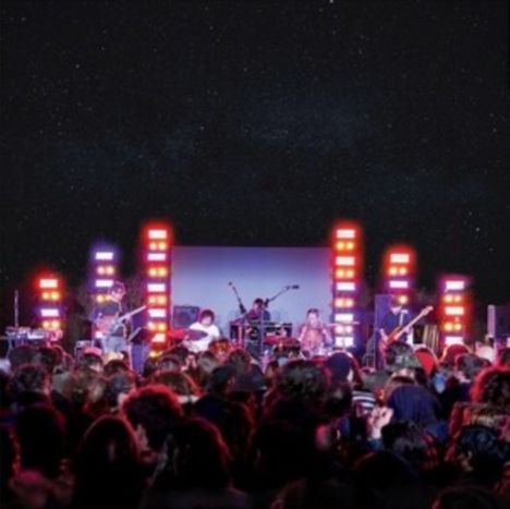 Menschenmenge vor einer Bühne; Band spielt unter Sternenhimmel, bunte Lichter umrahmen die Szenerie.