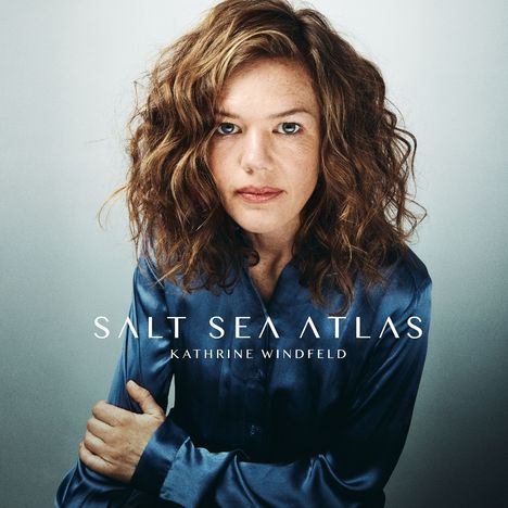 „SALT SEA ATLAS“, „KATHRINE WINDFELD“. Frau mit lockigem Haar und blauem Hemd schaut direkt nach vorne.
