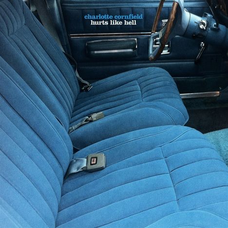 Text: "charlotte cornfield hurts like hell". Blaues Autositz-Interieur mit Sicherheitsgurten und Holzlenkrad.