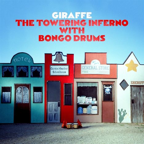 "GIRAFFE THE TOWERING INFERNO WITH BONGO DRUMS" in großer Schrift. Westlicher Straßenzug mit Hotel, Schule, Laden, Sheriff.