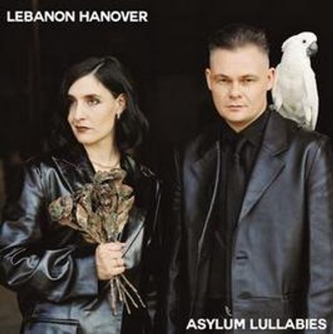 "LEBANON HANOVER", "ASYLUM LULLABIES". Zwei Menschen in schwarzen Ledermänteln, eine hält trockene Blumen, ein Kakadu auf der Schulter.