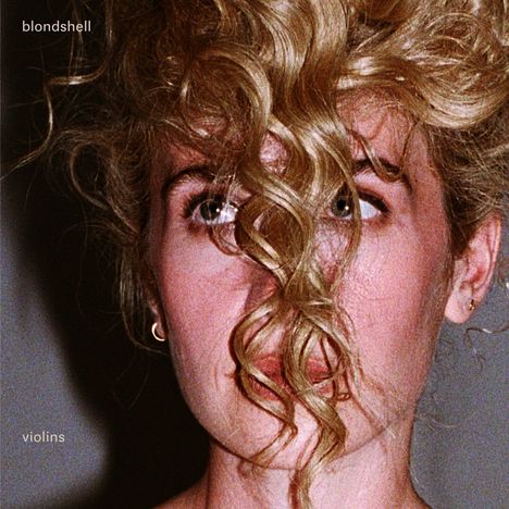 Text: "blondshell" oben links, "violins" unten links. Eine Frau mit lockigem, blondem Haar verdeckt teilweise ihr Gesicht.