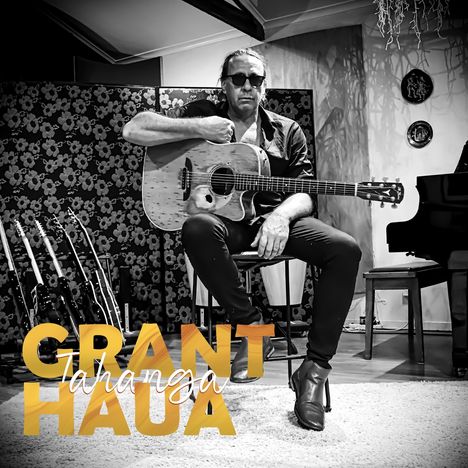 Text: "GRANT Tahanga HAUA". Ein Mann mit Sonnenbrille sitzt, hält eine Akustikgitarre. Im Hintergrund ein Blümchenmuster.