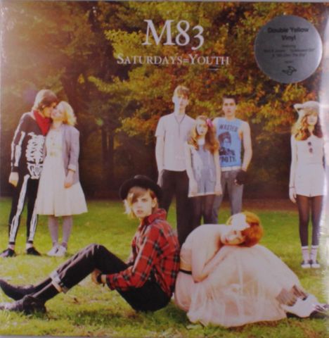 "M83, Saturdays=Youth" steht oben. Menschen in stilvollen, retro angehauchten Outfits auf einer grünen Wiese.