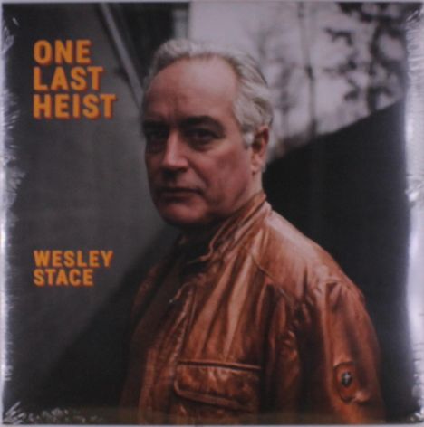 Titel: "ONE LAST HEIST", Name: "WESLEY STACE". Ein Mann in brauner Lederjacke blickt ernst, unscharfer Hintergrund mit Bäumen.